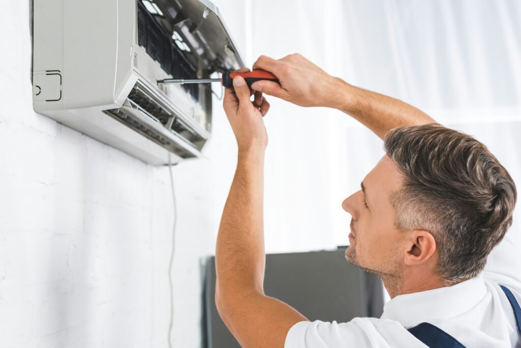 handsome adult man repairing air conditioner with screwdriver